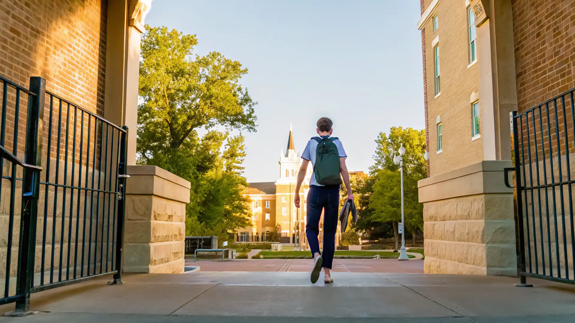 High school student walking toward a university campus entrance during summer